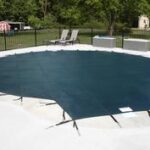 In-ground pool secured with a dark safety cover stretched tightly across the deck.