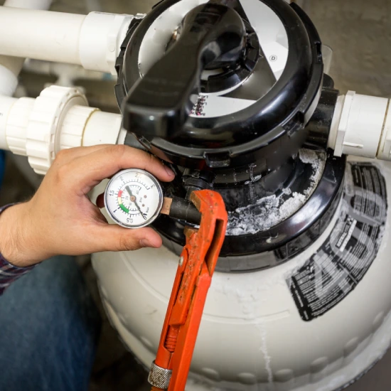 Technician tightening a pool filter clamp with a wrench while checking pressure on a sand filter system.