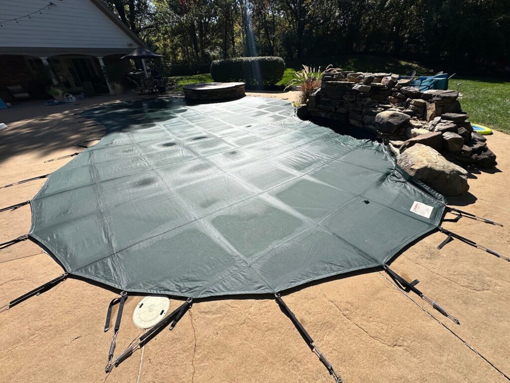 In-ground swimming pool secured with a fitted safety cover anchored to the surrounding pool deck.