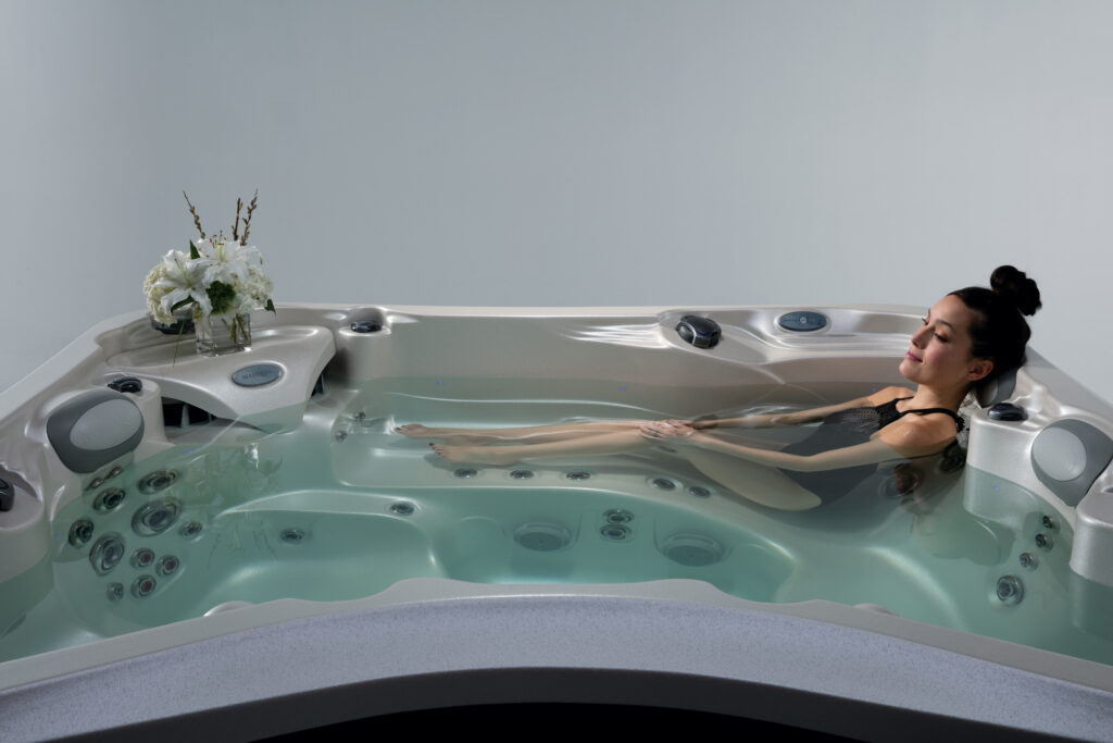 Woman reclining in a large Marquis spa hot tub, relaxing in the water with her head resting on the corner seat.