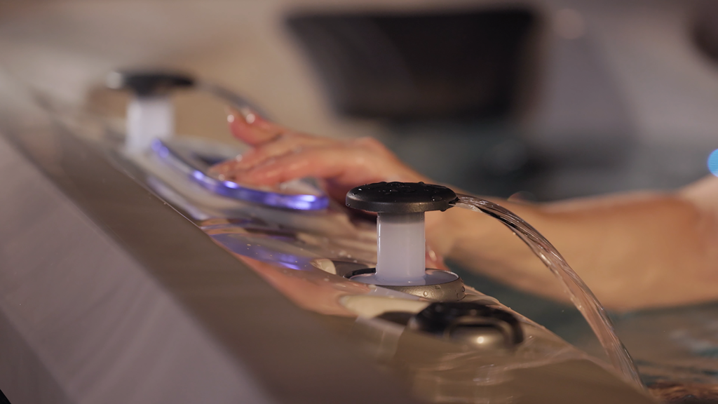 Hand adjusting the illuminated control panel on a modern hot tub spa.